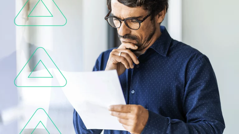 Empresário olhando para um papel em sua mão com expressão bastante preocupada