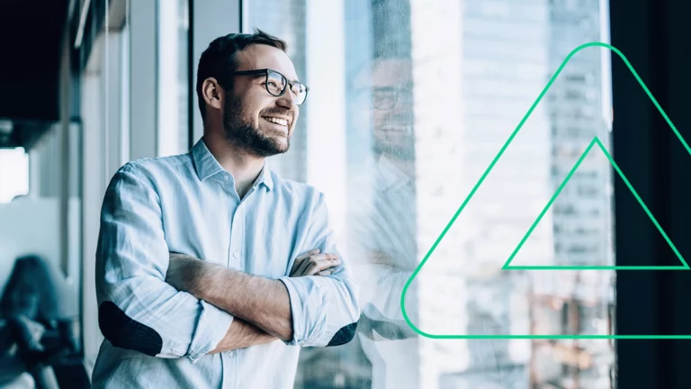 Empresário posando encostado na janela do seu escritório, sorrindo contente com o seu sucesso