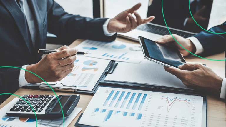 Mesa cheia de documentos e relatórios, com uma calculadora e um tablet visíveis, enquanto duas pessoas conversam sobre ROI
