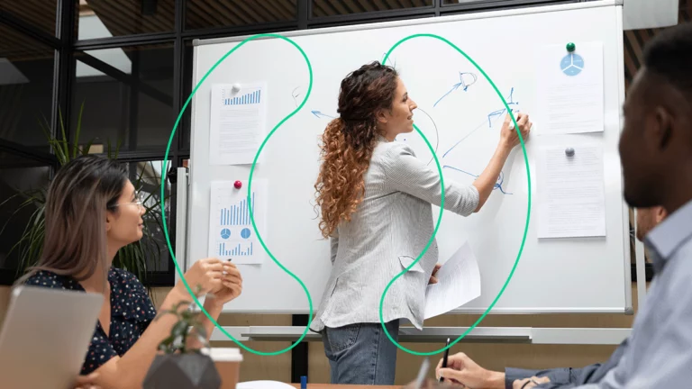 Mulher explicando para um grupo de pessoas como montar um e-commerce, usando um quadro-branco repleto de informações, relatórios e desenhos