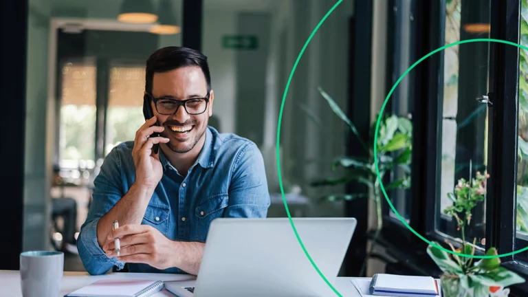Empreendedor em seu local de trabalho, falando no telefone sorrindo ao ver o sucesso do seu e-commerce
