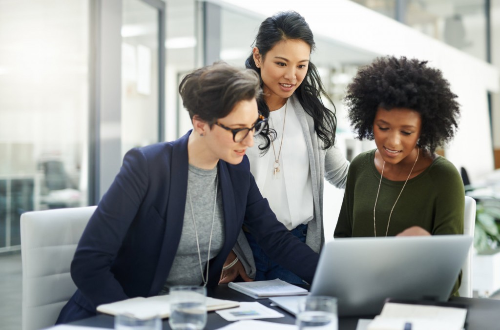 3 mulheres empreendedoras sorrindo e conversando sobre algo que estão olhando na tela do computador