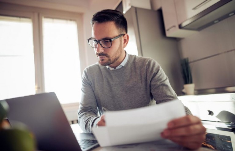 Empreendedor segurando documentos e olhando preocupado para a tela do computador, tentando entender o que muda com a NF-e 4.0