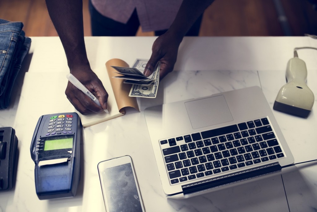 Empreendedor calculando sua apuração de lucro, em uma mesa com papéis, laptop, calculadora e celular espalhados
