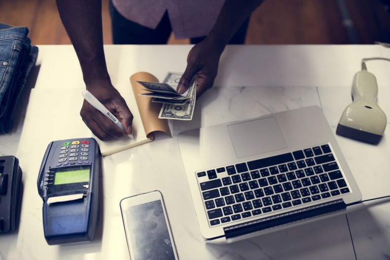 Empreendedor calculando sua apuração de lucro, em uma mesa com papéis, laptop, calculadora e celular espalhados