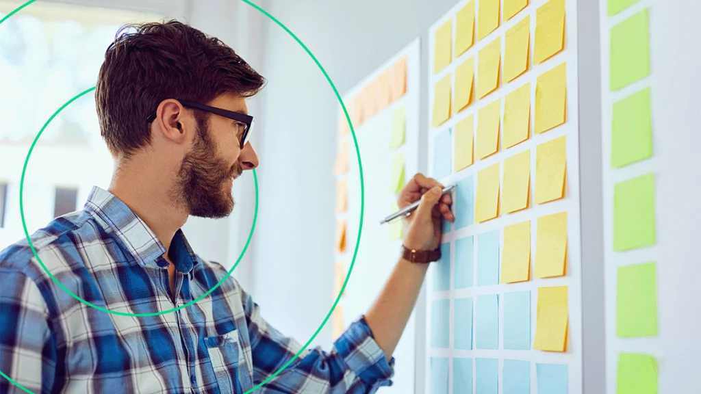 Homem planejando o marketing para o ano novo em um quadro cheio de notas adesivas