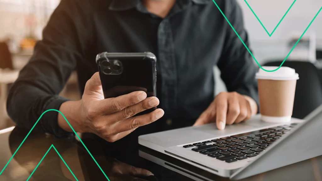 Pessoa utilizando um notebook ao mesmo tempo em que confere informações no celular, representando a presença omnichannel