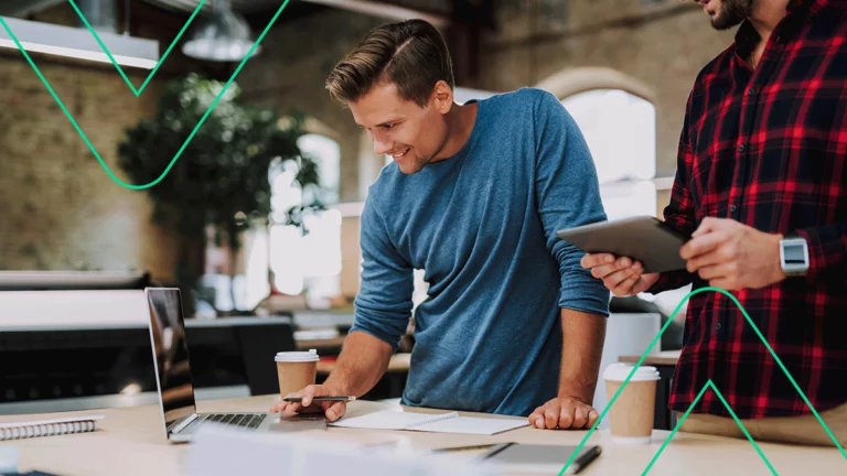 Dois colegas de trabalho analisando informações num tablet e num laptop sobre como vender mais no e-commerce para a Geração Z