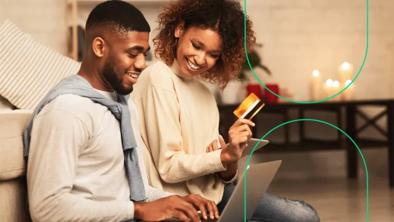 Casal fazendo compras na internet, uma pessoa segura o notebook e a outra um cartão de crédito