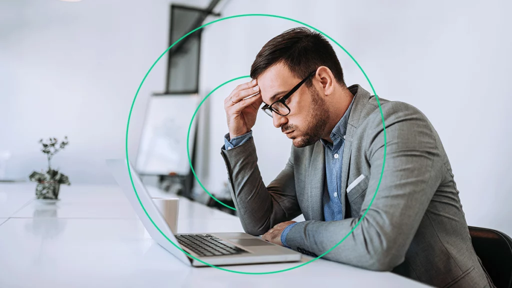 Homem frustrado olhando para o notebook com expressão de preocupação, pensando em como evitar calote dos clientes