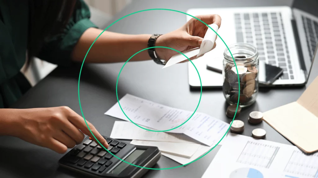 Pessoa somando valores de diversos comprovantes, totalizando o custo do produto