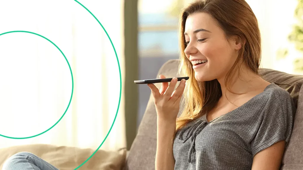 Mulher segurando o celular na frente da boca, falando na direção do microfone do aparelho