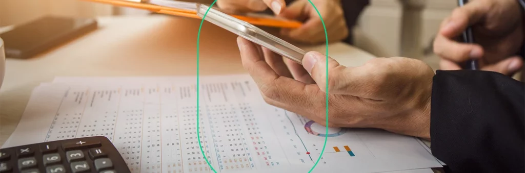 Close-up de mãos mexendo num celular em cima de uma mesa com vários relatórios de contas e impostos DIFAL