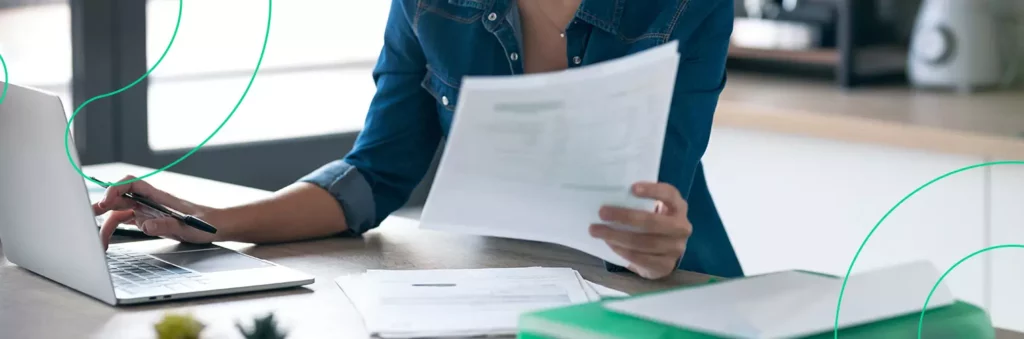 Empreendedora preenchendo uma nota fiscal avulsa em seu computador enquanto analisa documentos